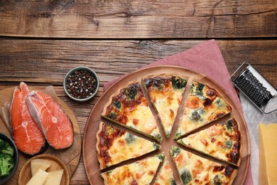 Delicious homemade quiche and ingredients on wooden table, flat lay