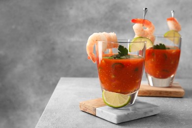 Tasty shrimp cocktail with sauce in glasses and lime on light grey table, space for text