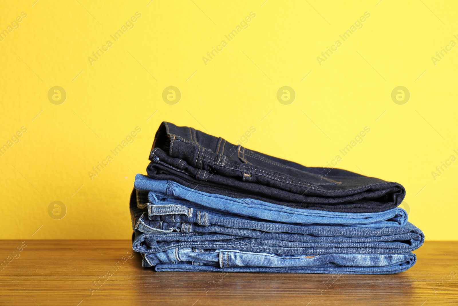 Photo of Stack of jeans on table against color background