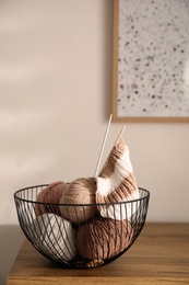 Yarn balls and knitting needles in metal basket on wooden table indoors, space for text. Creative hobby