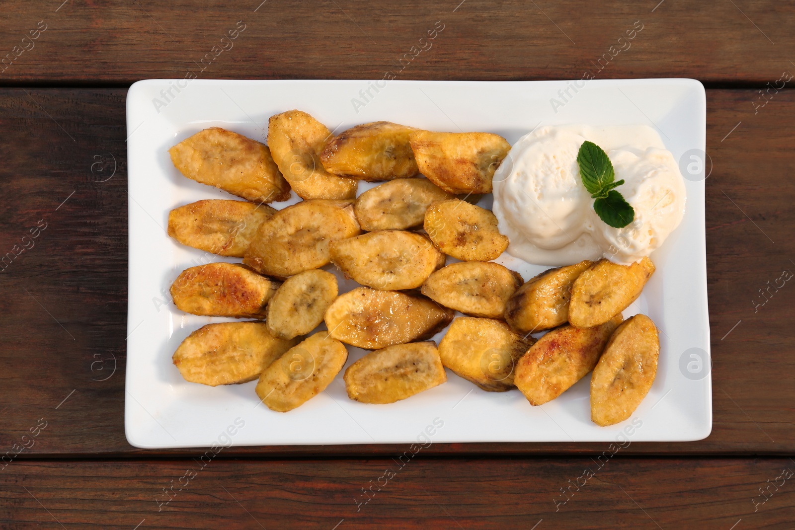 Photo of Tasty deep fried banana slices and ice cream with mint on wooden table, top view