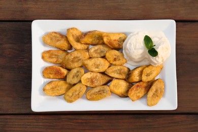 Photo of Tasty deep fried banana slices and ice cream with mint on wooden table, top view