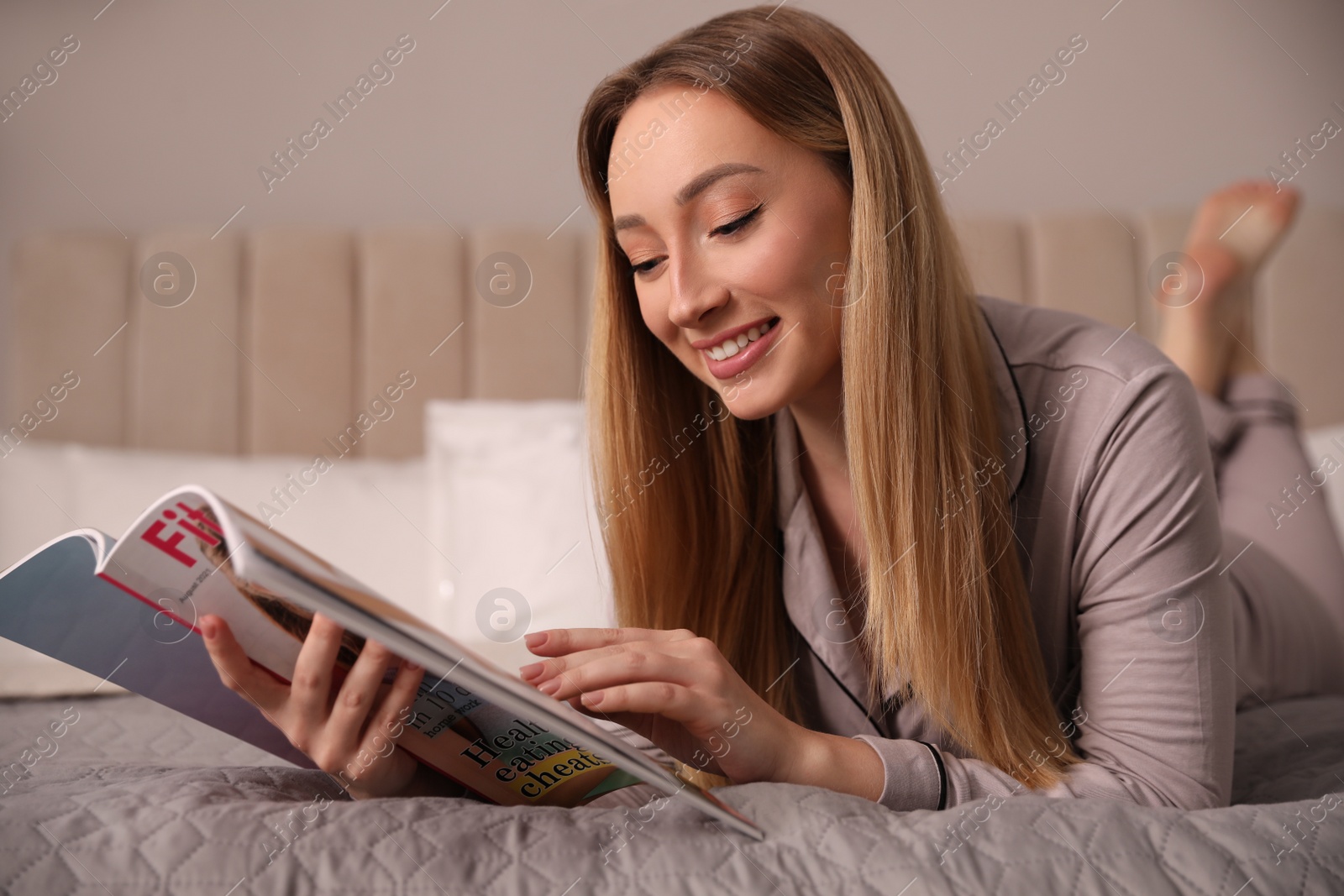 Photo of Happy woman reading magazine on bed indoors