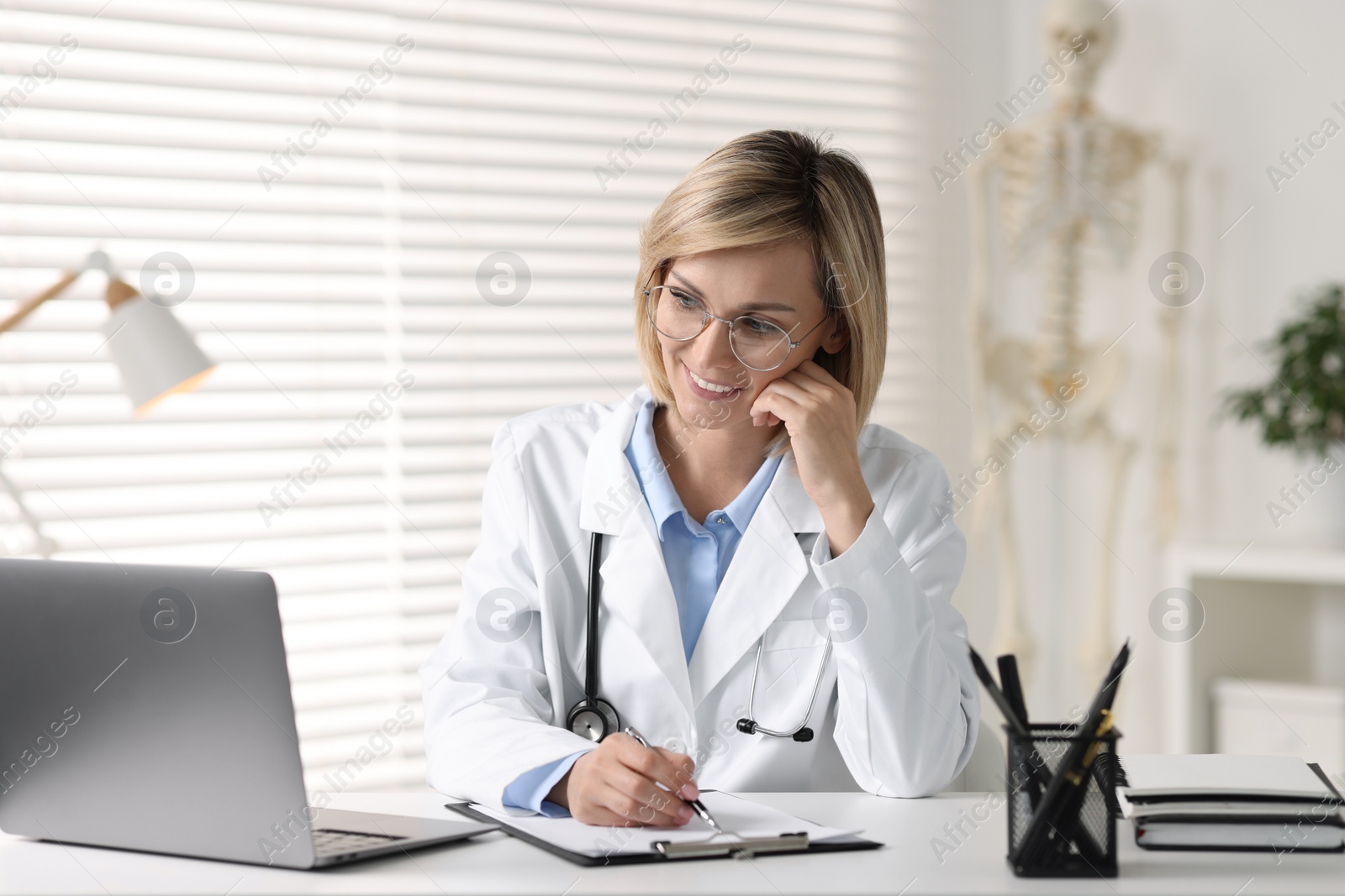 Photo of Smiling doctor with laptop having online consultation at table in office