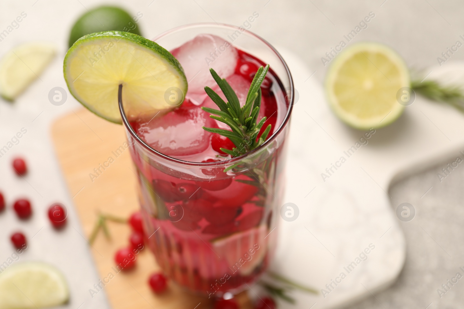 Photo of Tasty cranberry cocktail with rosemary and lime in glass on table, closeup