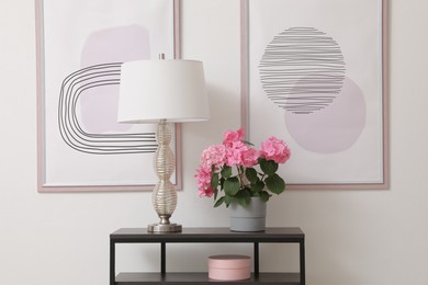 Photo of Console table with beautiful hydrangea flower and lamp near white wall in hallway. Interior design