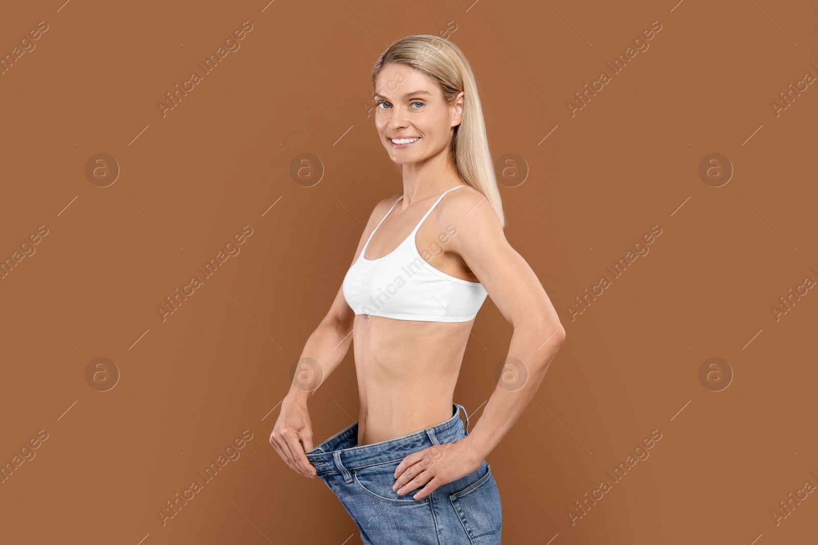 Photo of Slim woman wearing big jeans on brown background. Weight loss