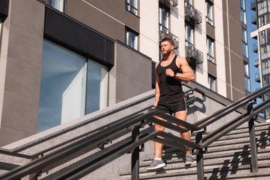 Photo of Man running down stairs outdoors on sunny day, low angle view. Space for text
