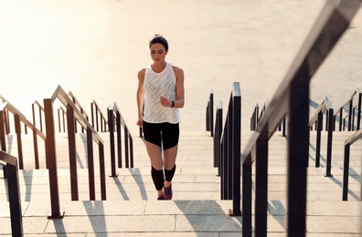 Photo of Sporty young woman running upstairs on sunny day