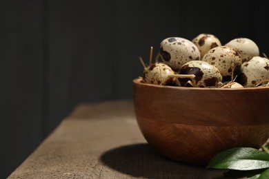 Bowl with quail eggs and green leaves on wooden table, closeup. Space for text