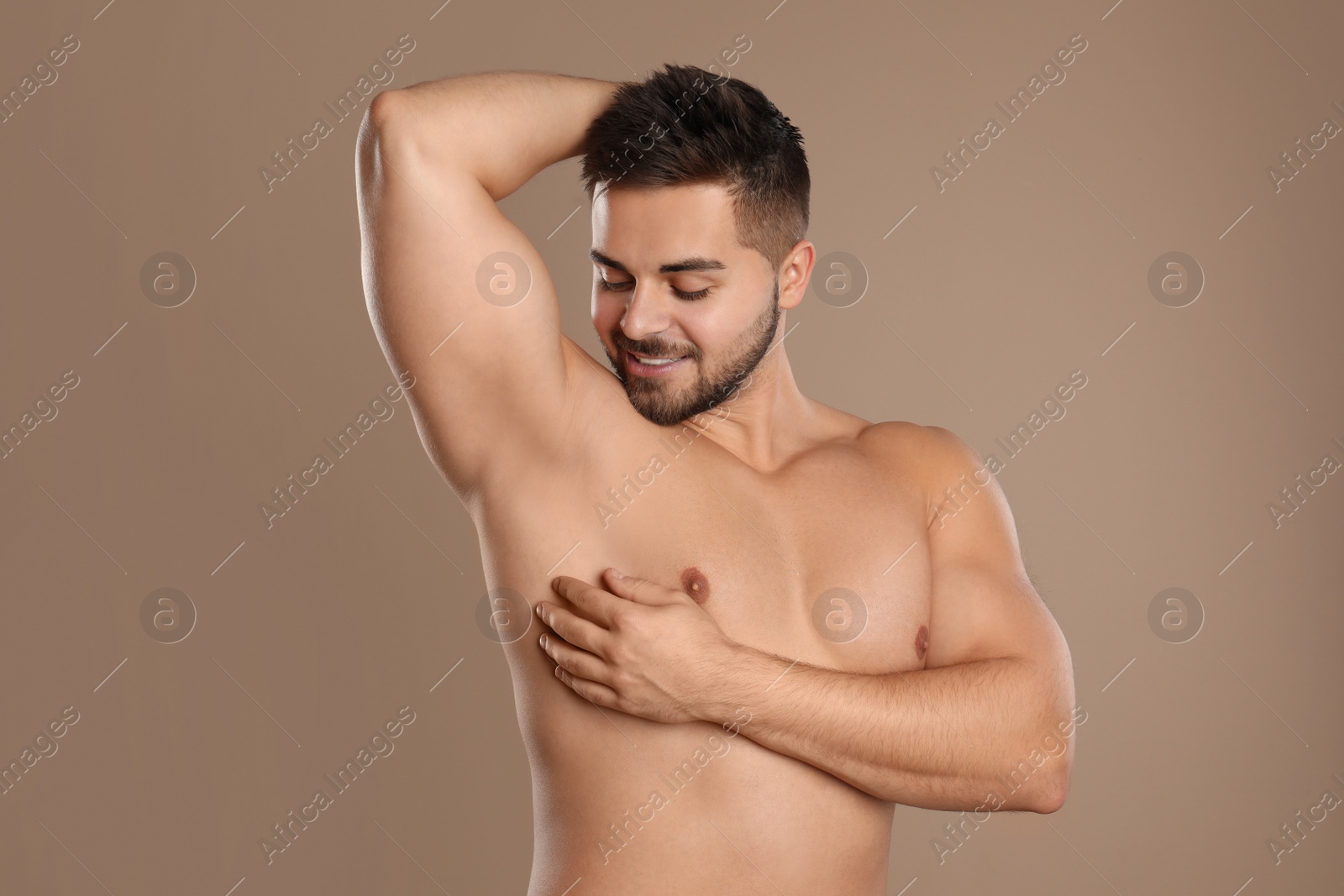 Photo of Young man showing hairless armpit after epilation procedure on brown background