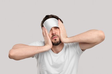 Tired man with sleep mask on light grey background. Insomnia problem