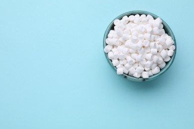Photo of Bowl with delicious marshmallows on light blue background, top view. Space for text