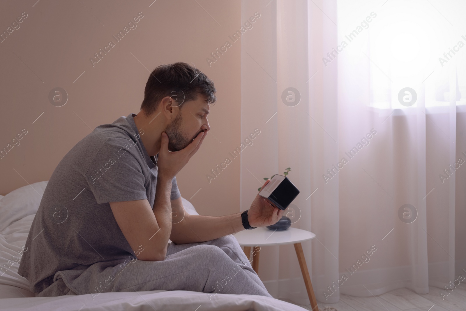 Photo of Sleepy man with clock in bed at home