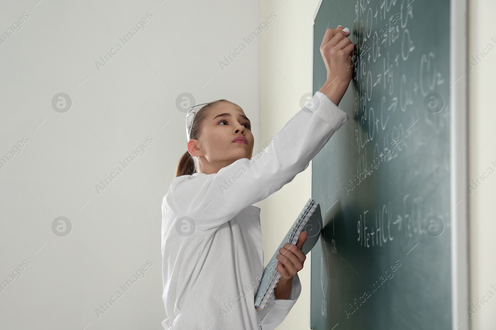 Photo of Schoolgirl writing chemistry formula on blackboard in class