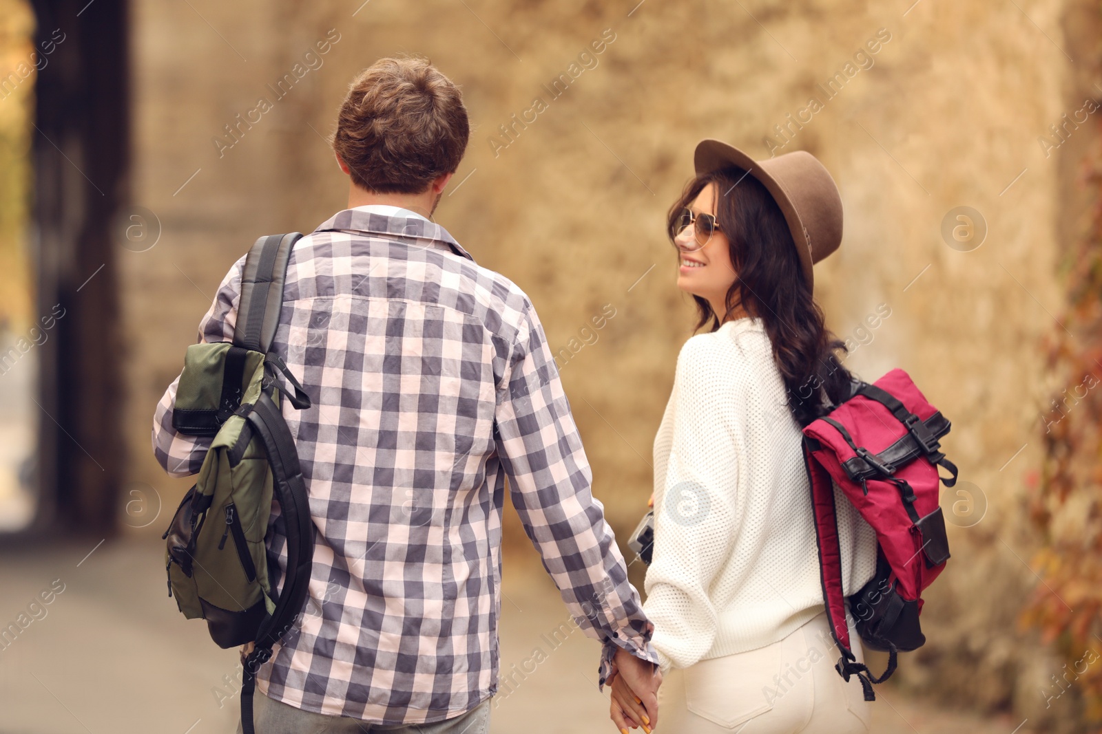 Photo of Couple of travelers with backpacks on city street, back view