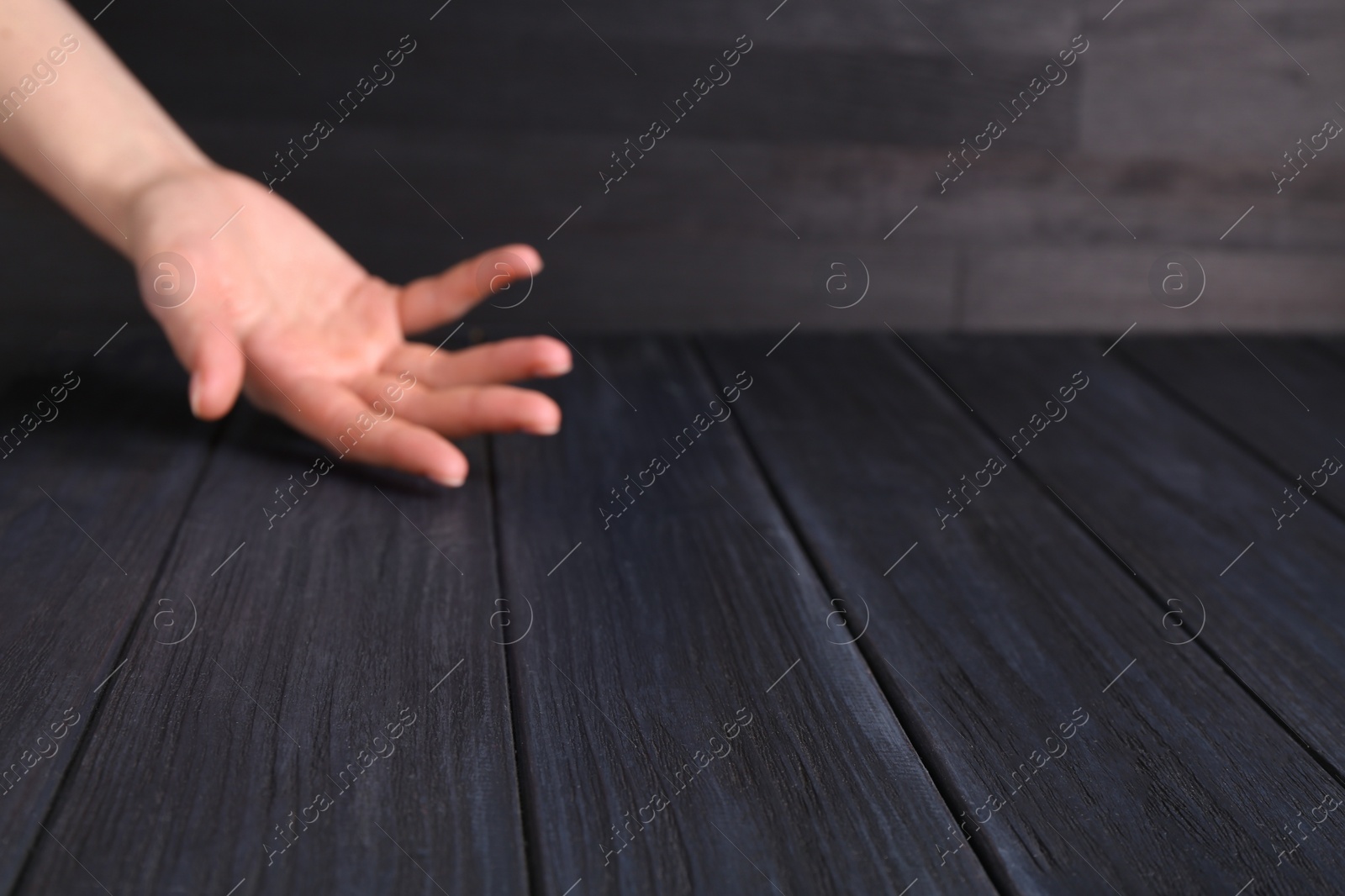 Photo of Woman holding hand above black wooden table, selective focus. Space for text
