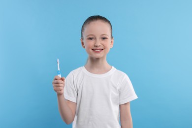 Photo of Happy girl holding toothbrush on light blue background
