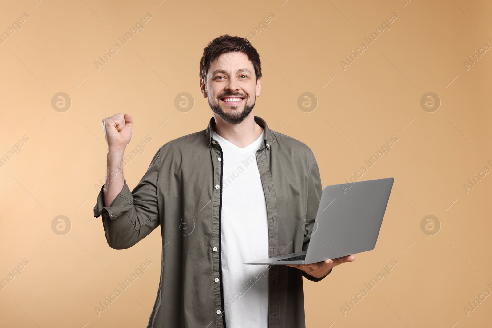 Photo of Happy man with laptop on beige background