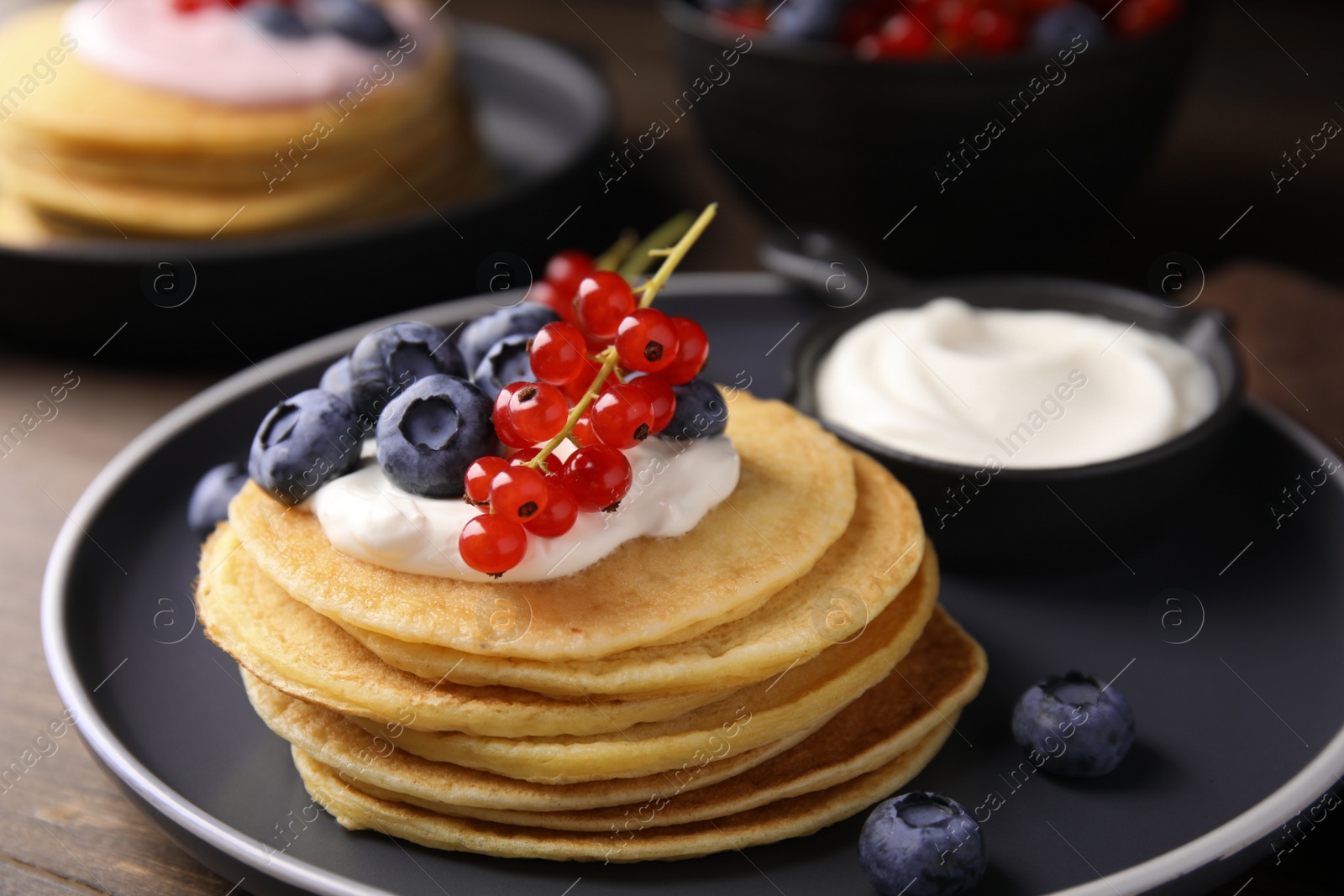 Photo of Tasty pancakes with natural yogurt, blueberries and red currants on wooden table