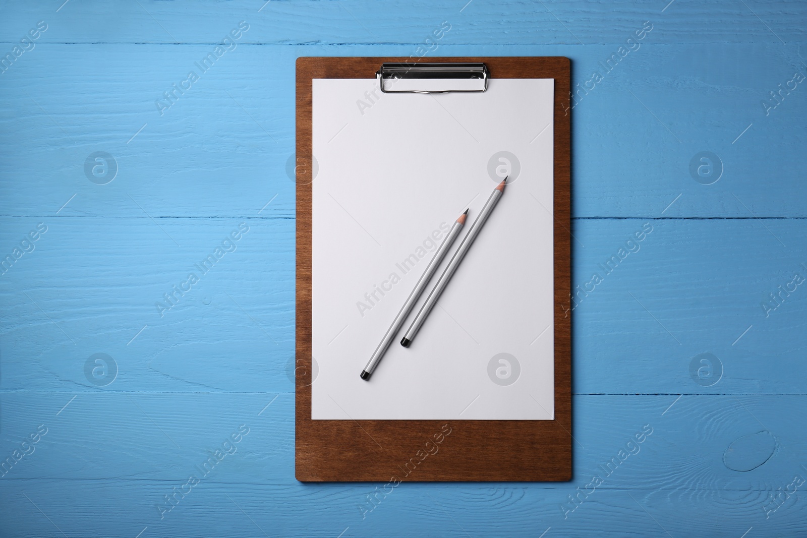 Photo of Clipboard with sheet of paper and pencils on light blue wooden table, top view