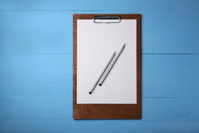 Clipboard with sheet of paper and pencils on light blue wooden table, top view