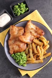 Photo of Tasty fish, chips, sauce and peas on grey table, flat lay