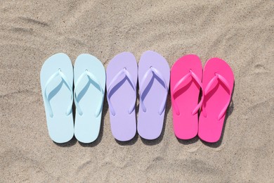 Photo of Stylish colorful flip flops on sand outdoors, flat lay