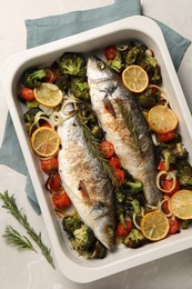 Photo of Delicious fish with vegetables and lemon in baking dish on light marble table, top view