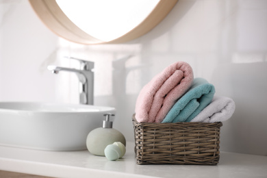 Photo of Basket with fresh towels, soap dispenser and bath bombs on countertop indoors