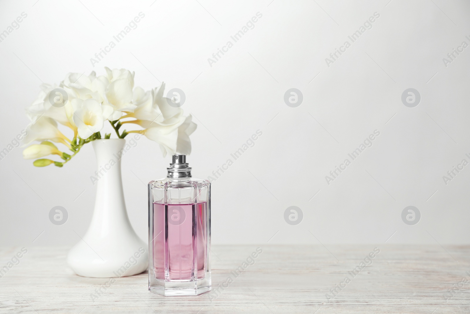 Photo of Bottle of perfume and vase with flowers on table against light background