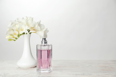 Photo of Bottle of perfume and vase with flowers on table against light background