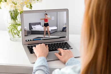 Image of Woman watching morning exercise video on laptop at table, closeup
