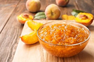 Photo of Bowl with tasty peach jam and fresh fruit on wooden table