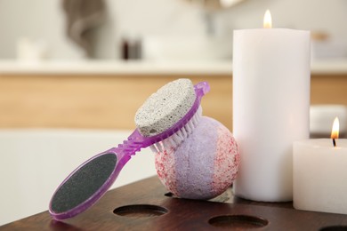 Photo of Pedicure tool with pumice stone and foot file near burning candles on wooden caddy in bathroom