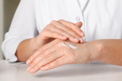 Photo of Dermatologist testing cosmetic product at white table, closeup