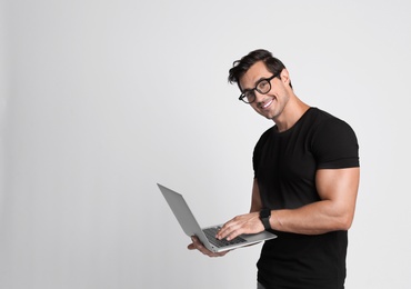 Handsome young man with laptop on grey background. Space for text