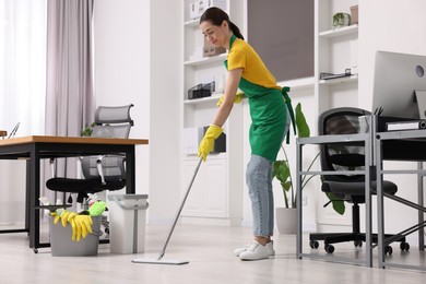 Photo of Cleaning service worker washing floor with mop. Bucket with supplies in office