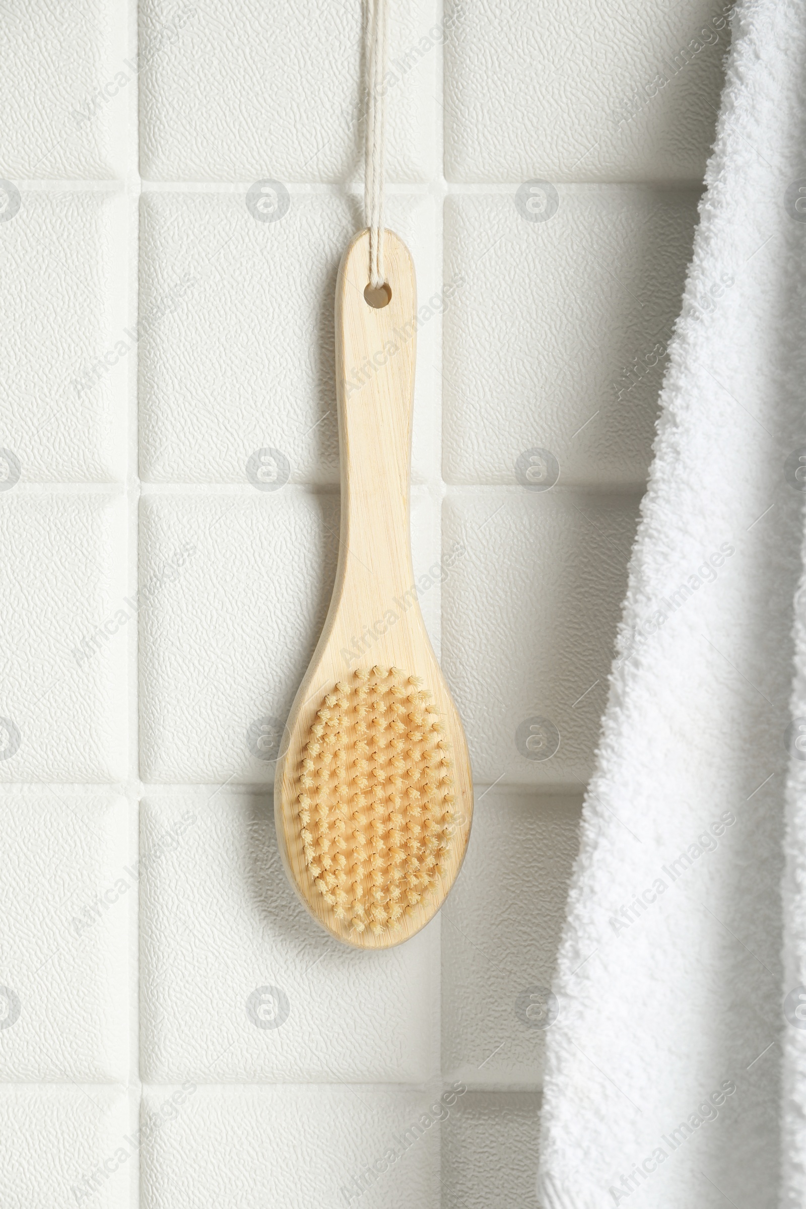 Photo of Bath accessories. Bamboo brush and terry towel on white tiled wall