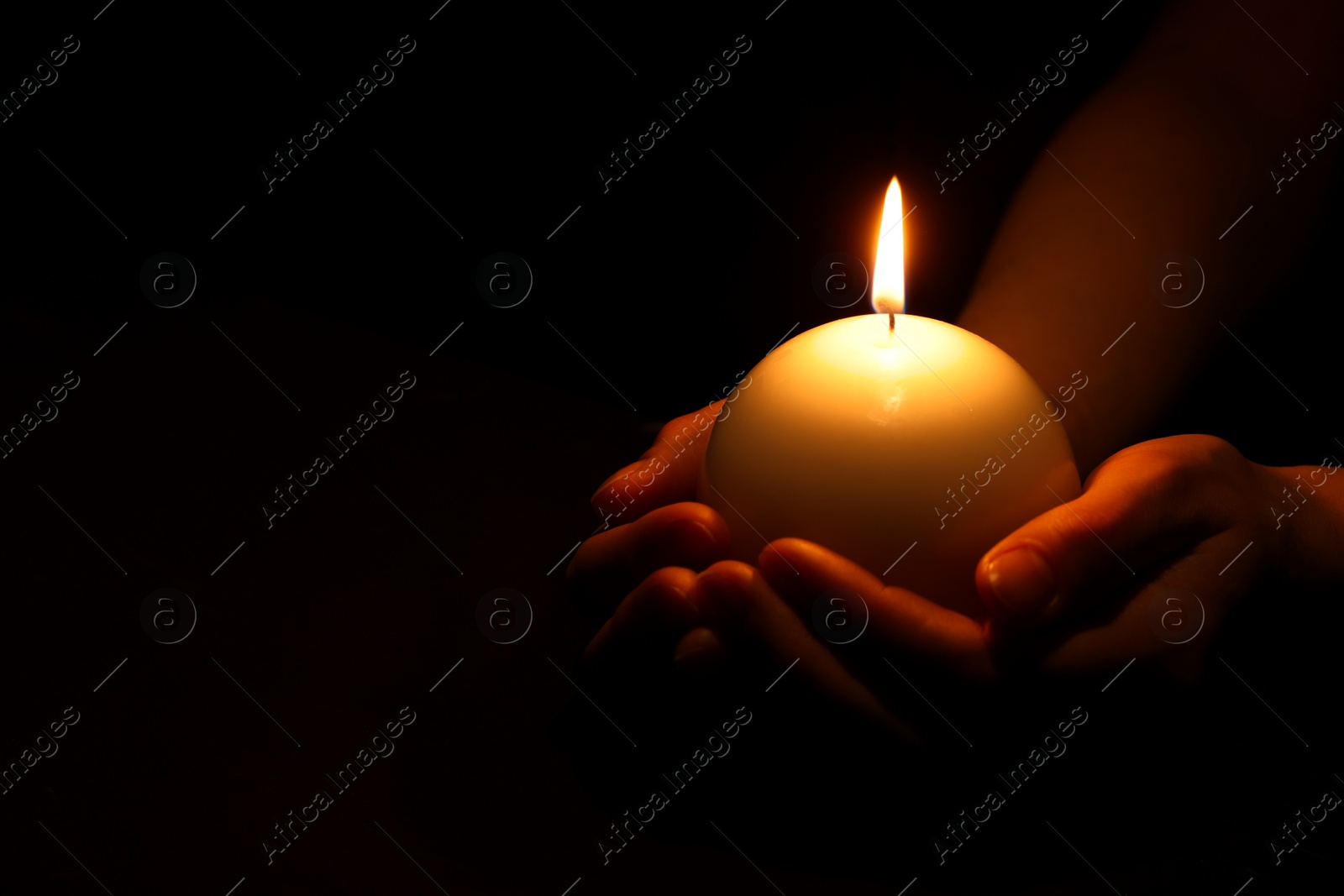 Photo of Woman holding burning candle in hands on black background, closeup. Space for text