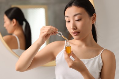 Photo of Beautiful young woman with bottle of cosmetic serum in bathroom