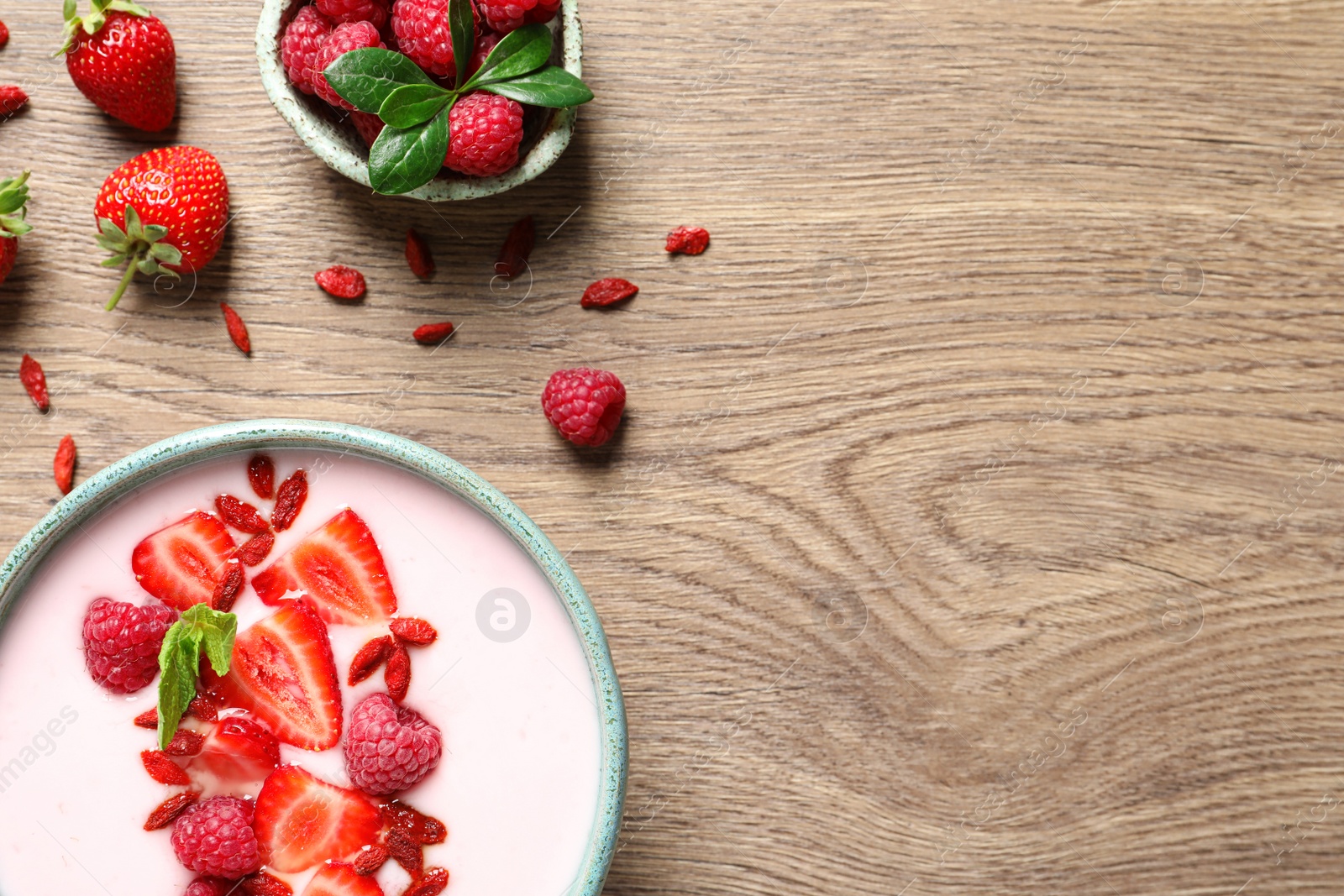 Photo of Smoothie bowl with goji berries on wooden table, flat lay. Space for text