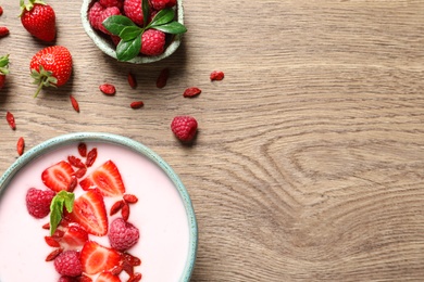 Photo of Smoothie bowl with goji berries on wooden table, flat lay. Space for text