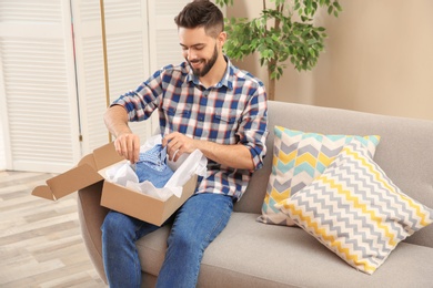 Photo of Young man opening parcel on sofa at home