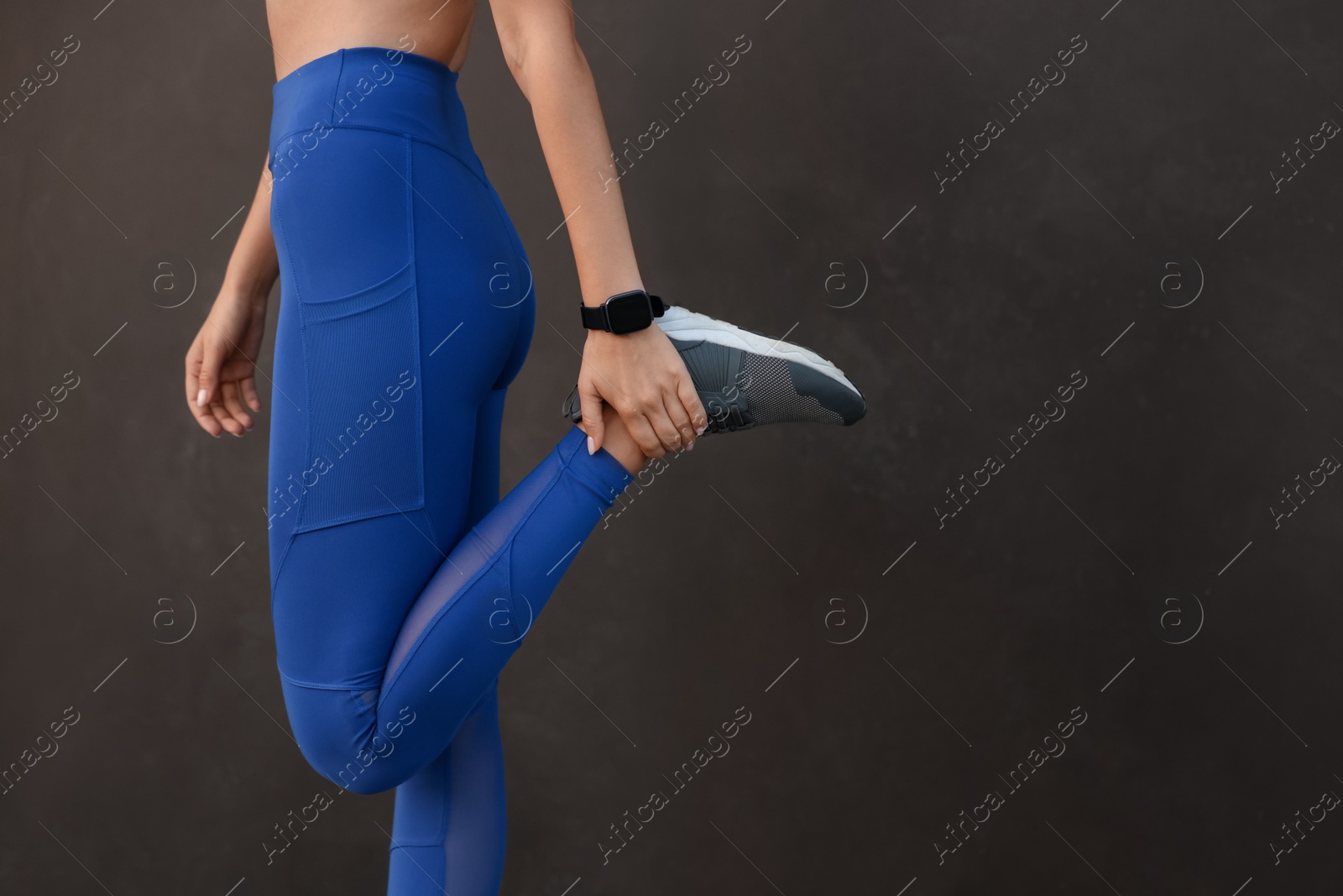 Photo of Woman in stylish sportswear doing exercises near black wall, closeup. Space for text