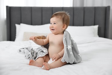 Happy baby boy with blanket and rattle sitting on bed at home