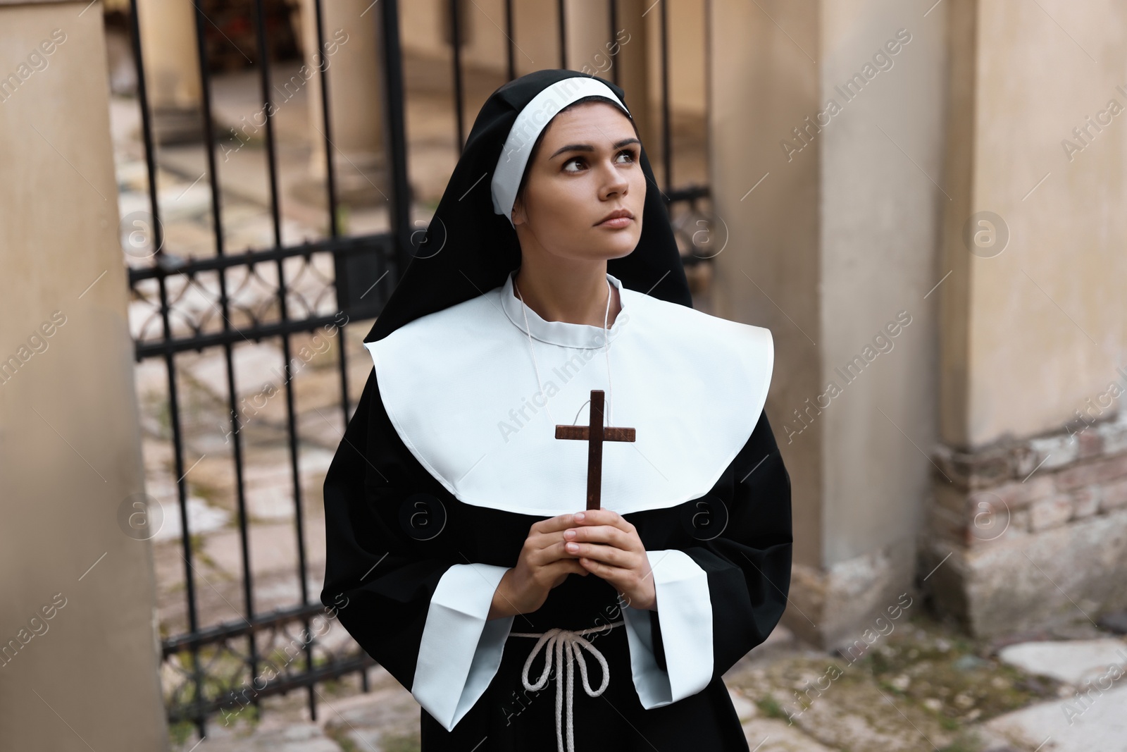 Photo of Young nun with Christian cross near building outdoors