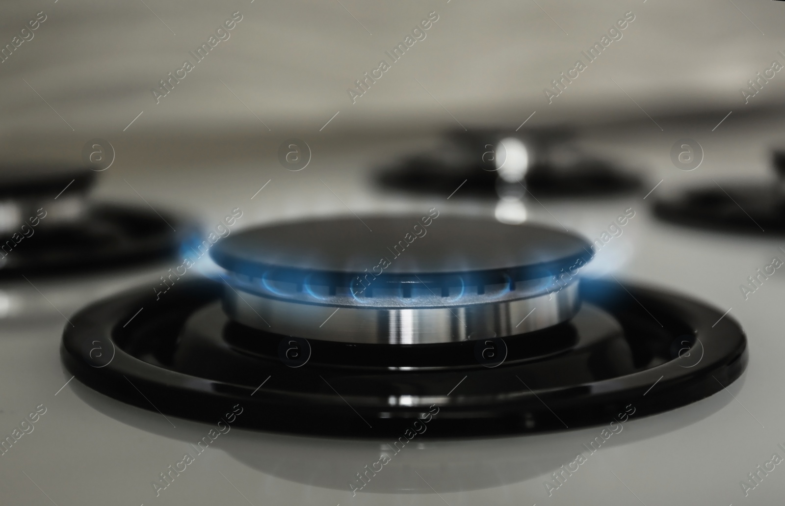 Photo of Gas burner with blue flame on modern stove, closeup