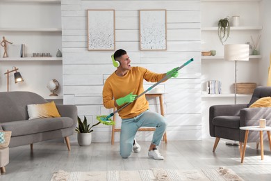 Photo of Man in headphones with mop singing while cleaning at home