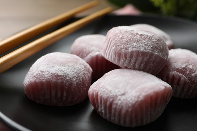 Photo of Delicious mochi and chopsticks on black plate, closeup. Traditional Japanese dessert